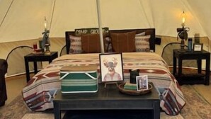 A tent with a bed, a small table, and two bedside tables with lamps.