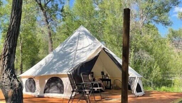 A large, A-frame tent with a wooden deck, surrounded by trees.