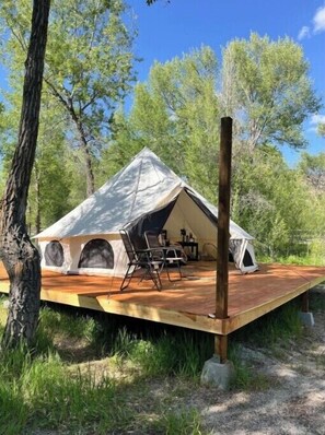 A large, A-frame tent with a wooden deck, surrounded by trees.