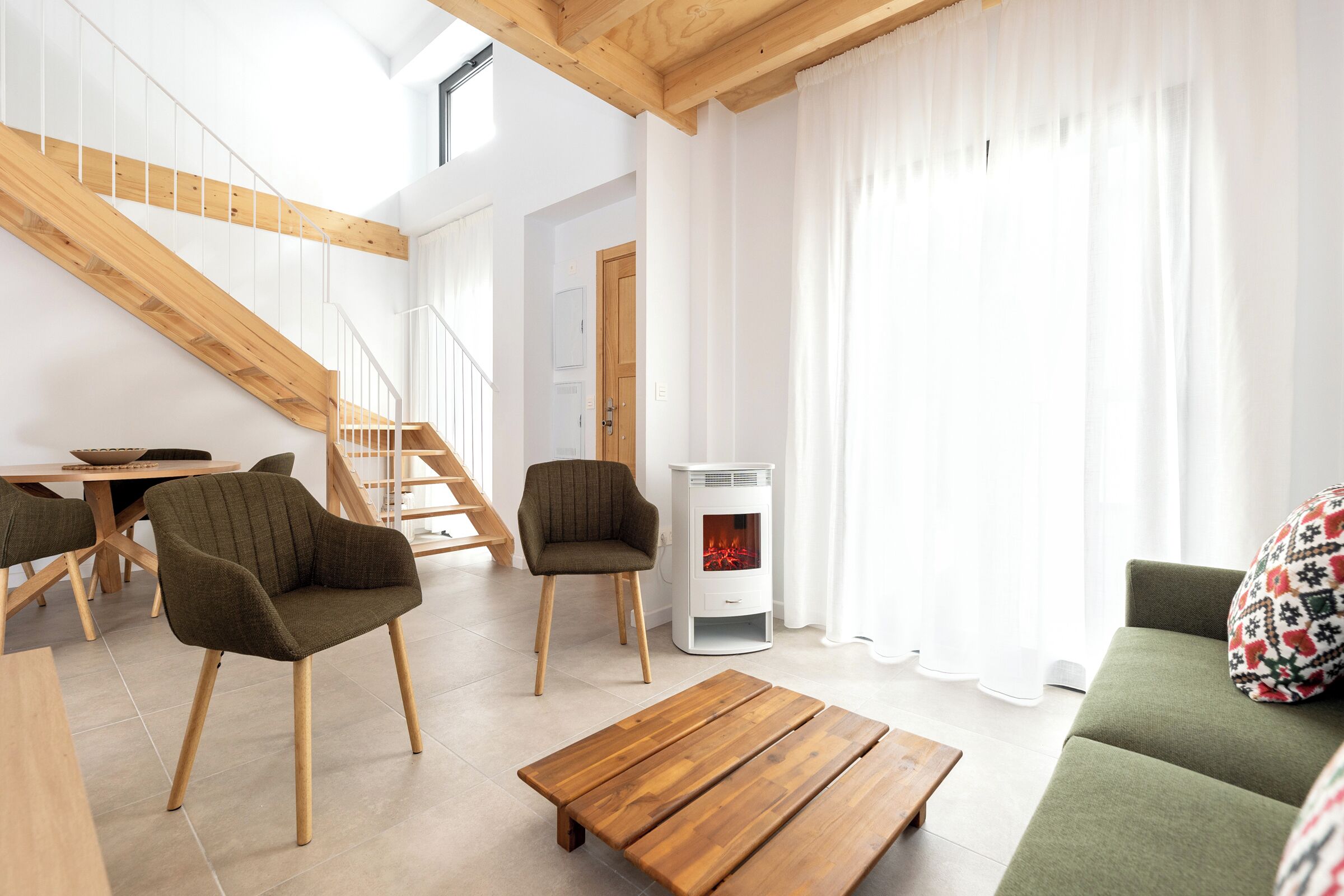 A modern living room with a wooden staircase, two armchairs, a sofa, and a fireplace.