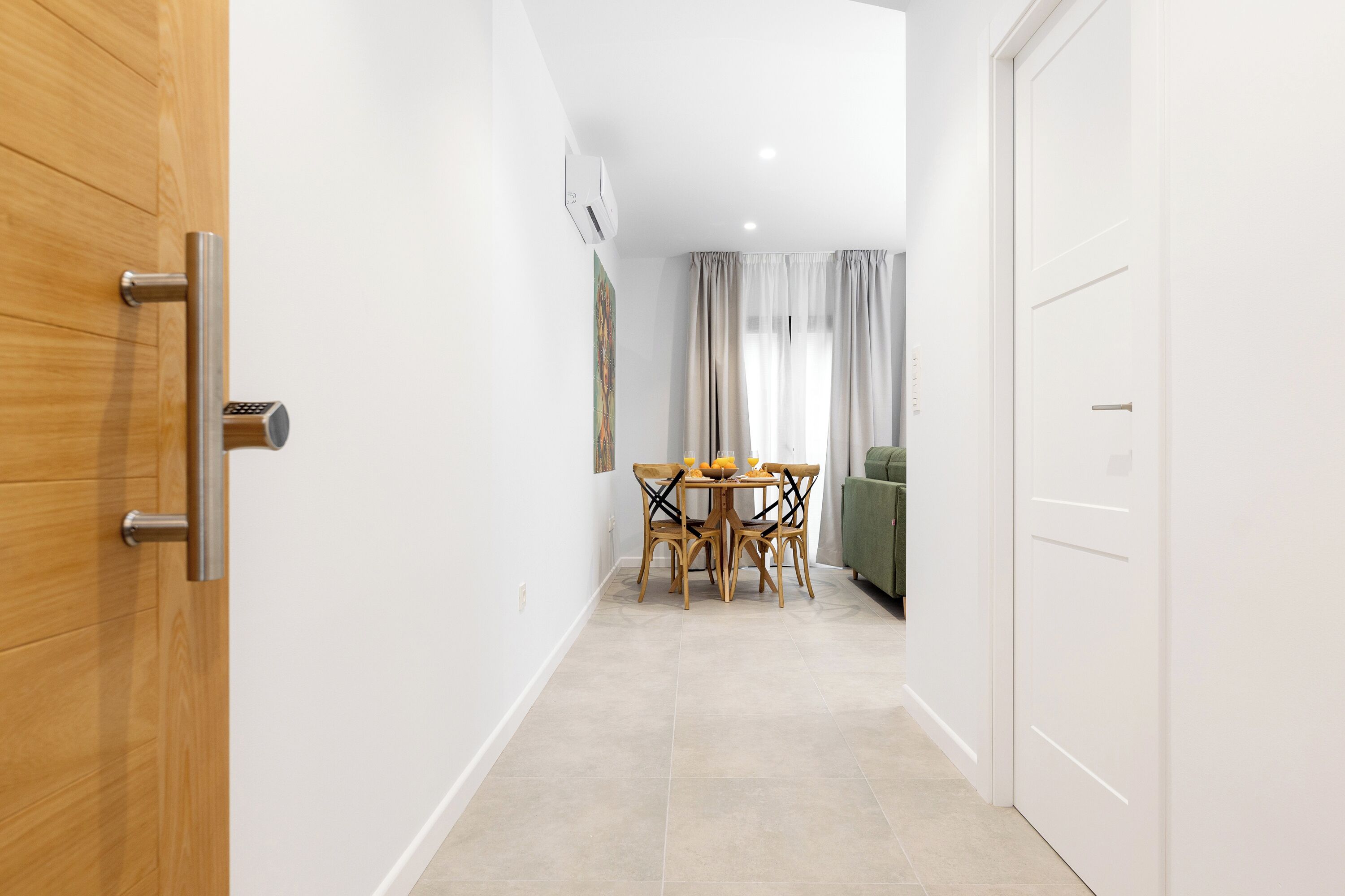 Un couloir avec une porte en bois, un coin repas avec une table et des chaises, et un canapé vert.
