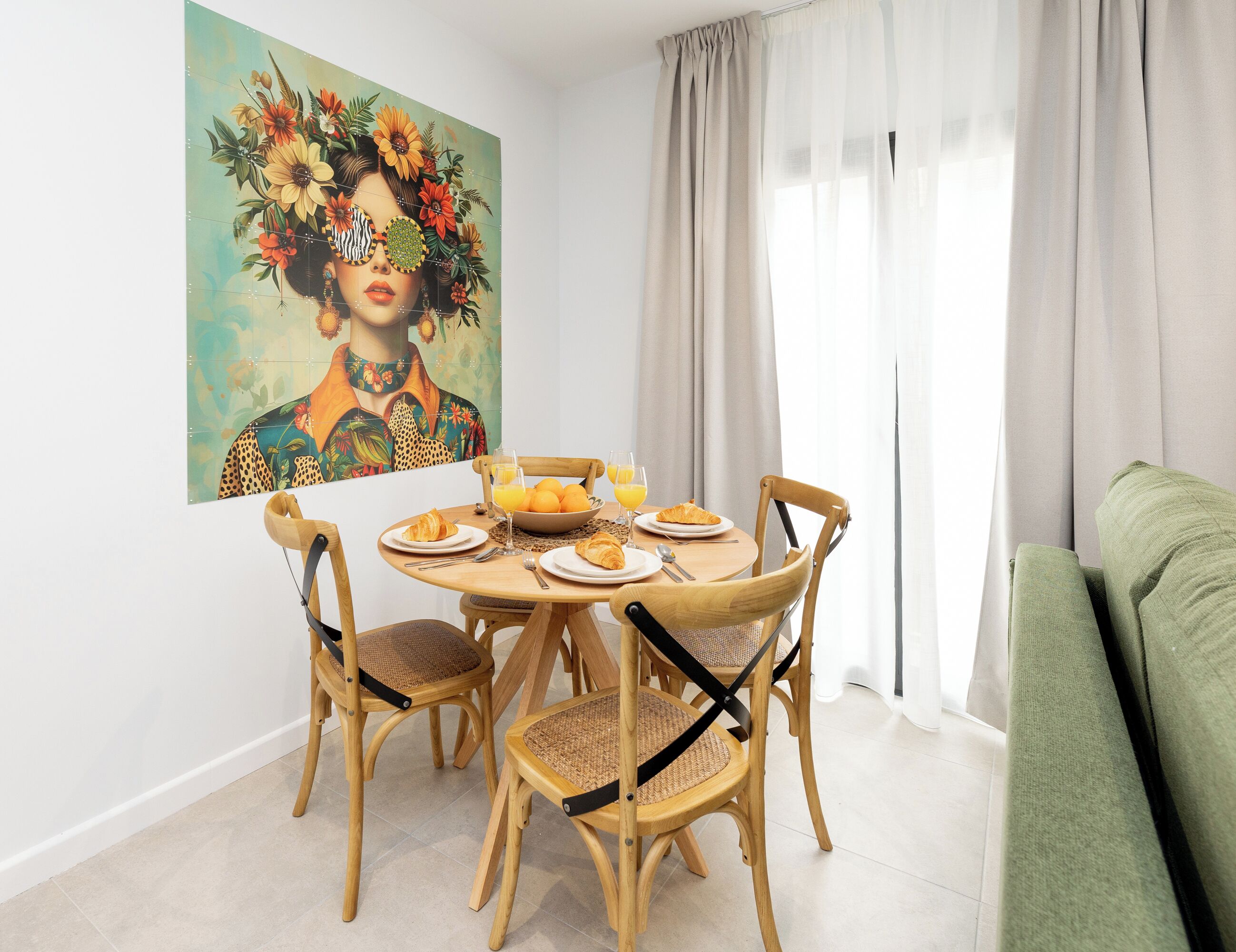 A dining area with a round wooden table, four chairs, and a painting on the wall.
