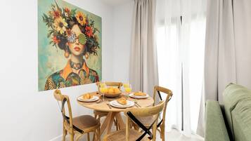 A dining area with a round wooden table, four chairs, and a painting on the wall.