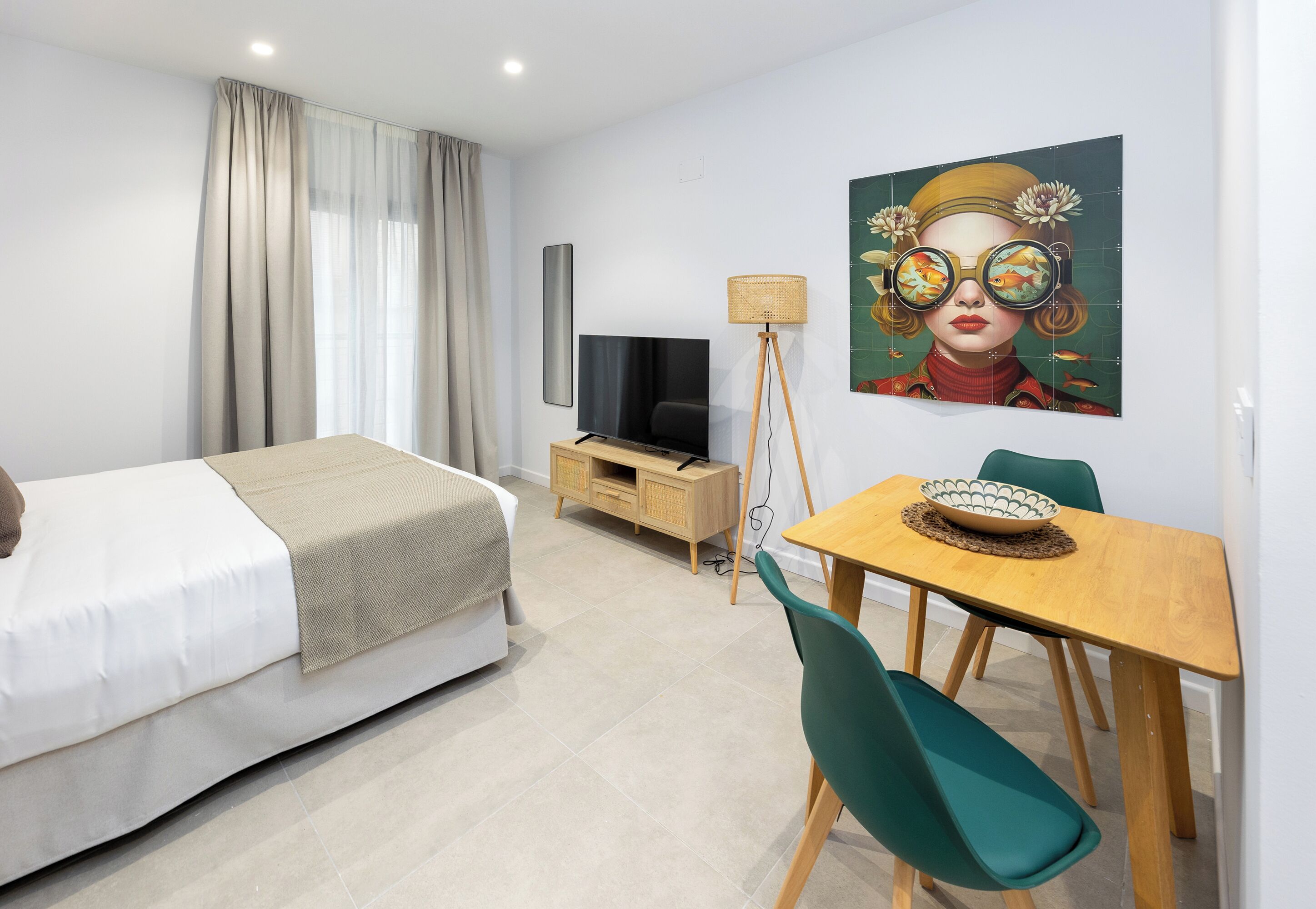 A modern hotel room with a bed, a TV, a dining table with chairs, and a painting on the wall.