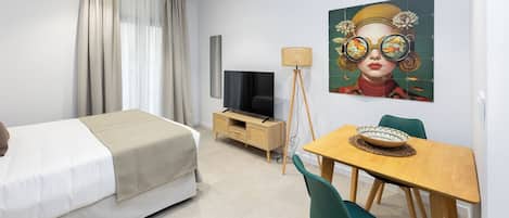 A modern hotel room with a bed, a TV, a dining table with chairs, and a painting on the wall.