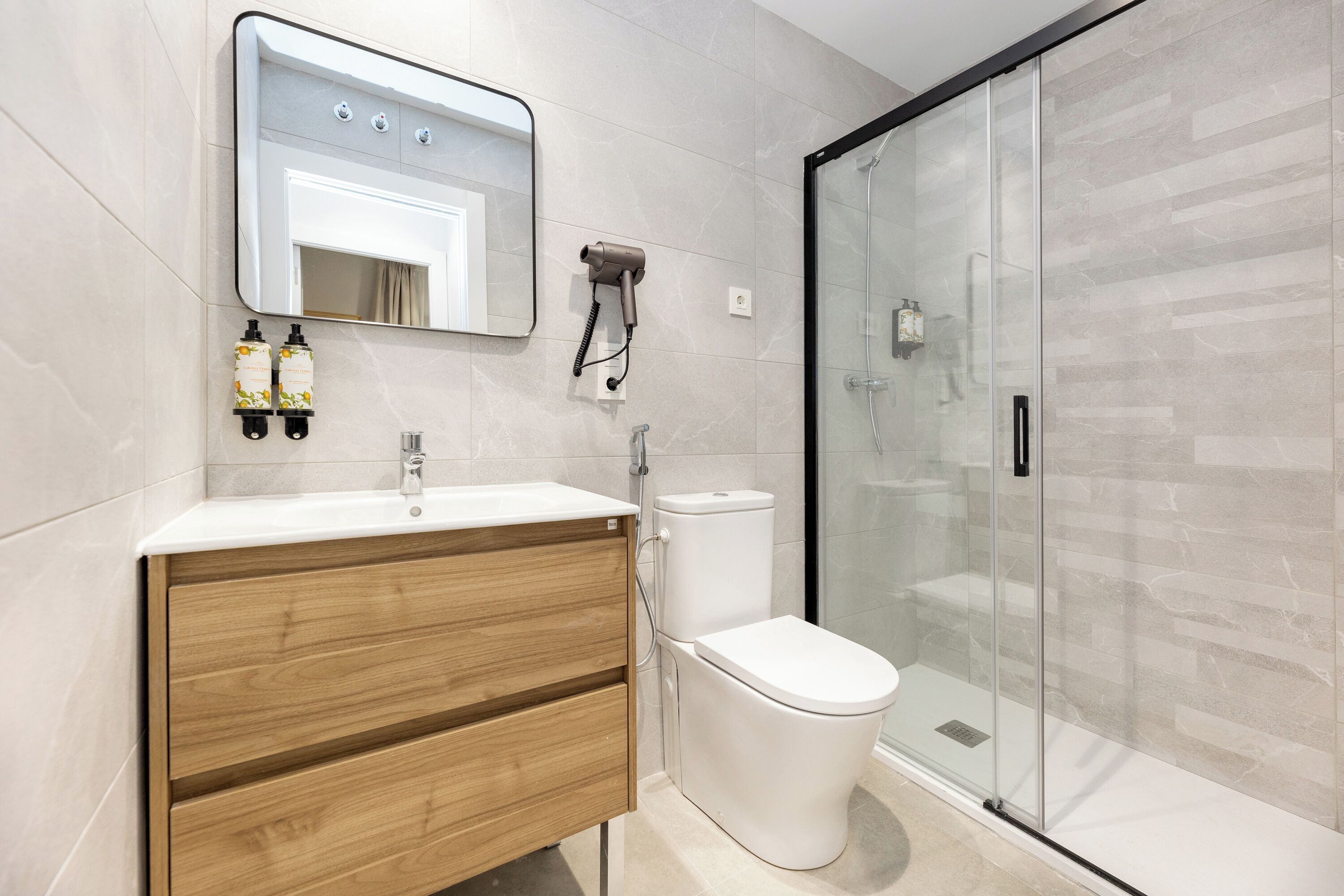 A modern bathroom with a wooden vanity, a white sink, a toilet, and a glass shower enclosure.
