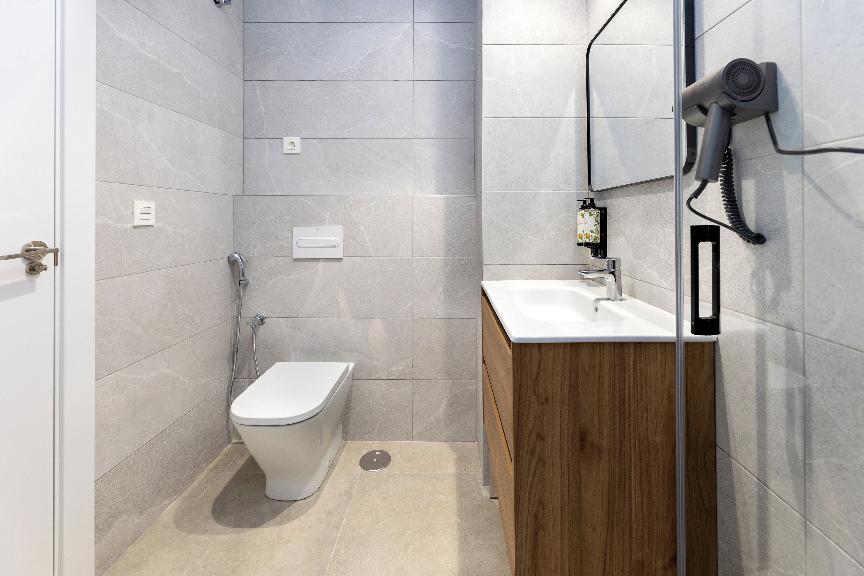 Un baño moderno con inodoro, lavamanos y secador de pelo fijado en la pared.