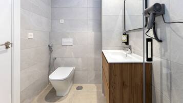 Un baño moderno con inodoro, lavamanos y secador de pelo fijado en la pared.