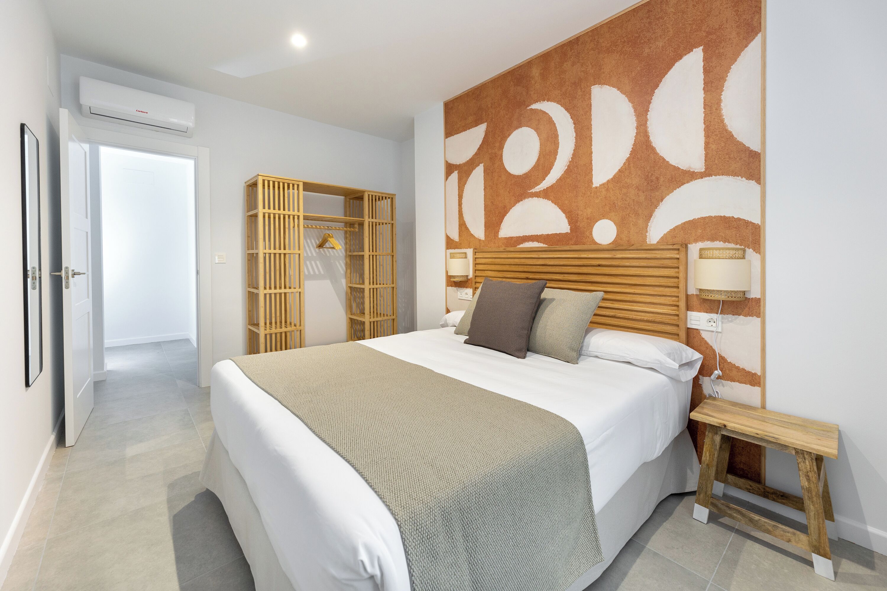 A modern bedroom with a large bed, wooden headboard, bedside lamps, and a built-in wardrobe.