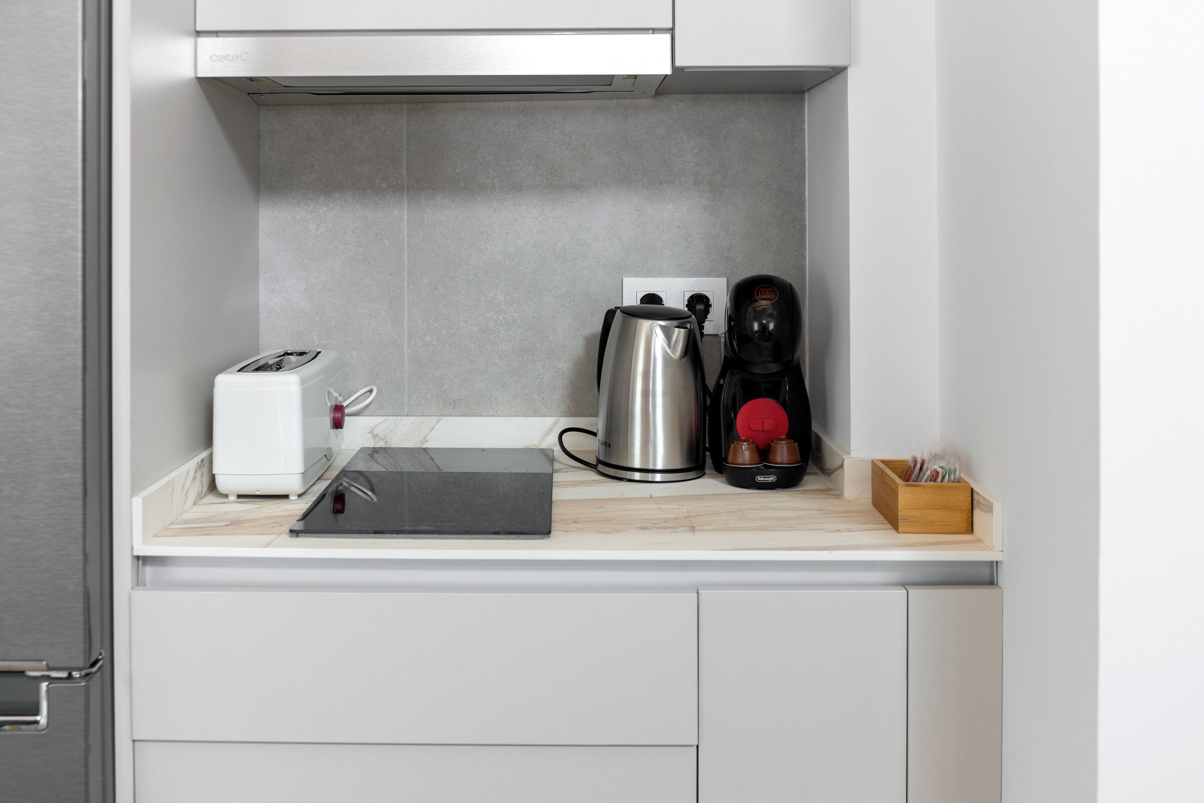 A compact kitchen with a toaster, a kettle, and a coffee maker on a countertop.