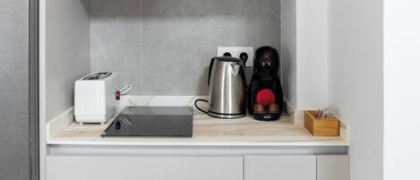 A compact kitchen with a toaster, a kettle, and a coffee maker on a countertop.