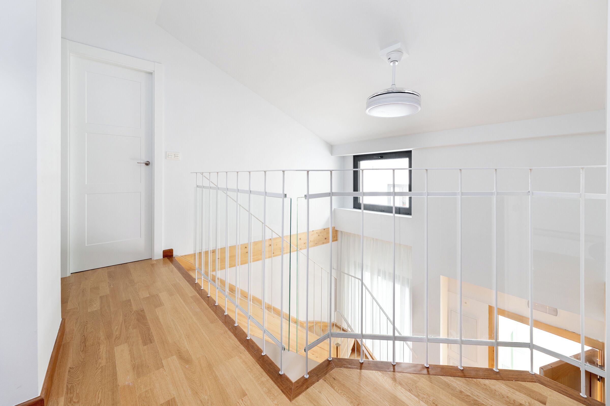A staircase with wooden steps and white railings, leading to a landing with a window.