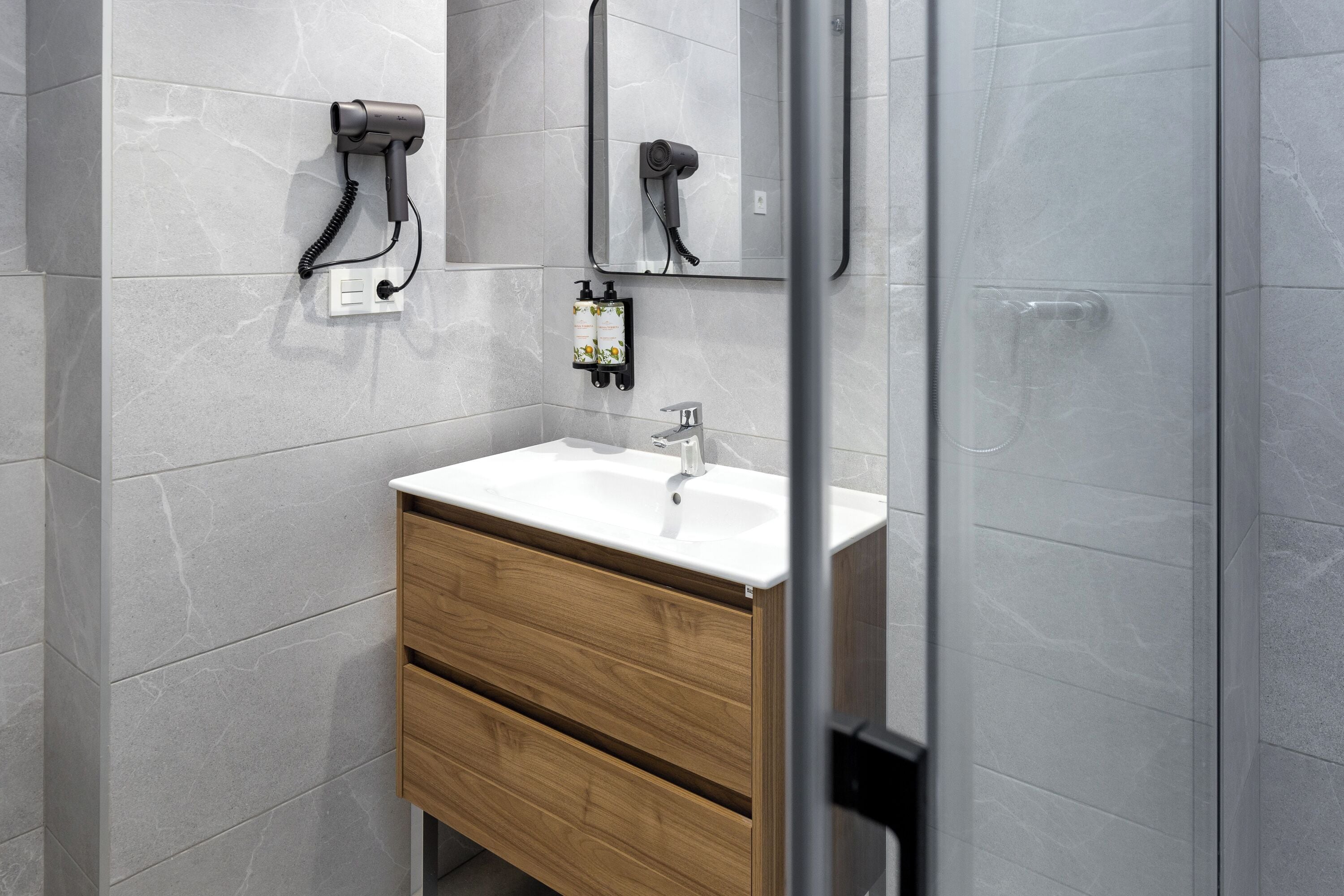 A modern bathroom with a white sink, wooden cabinet, and a hairdryer mounted on the wall.