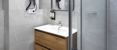 A modern bathroom with a white sink, wooden cabinet, and a hairdryer mounted on the wall.