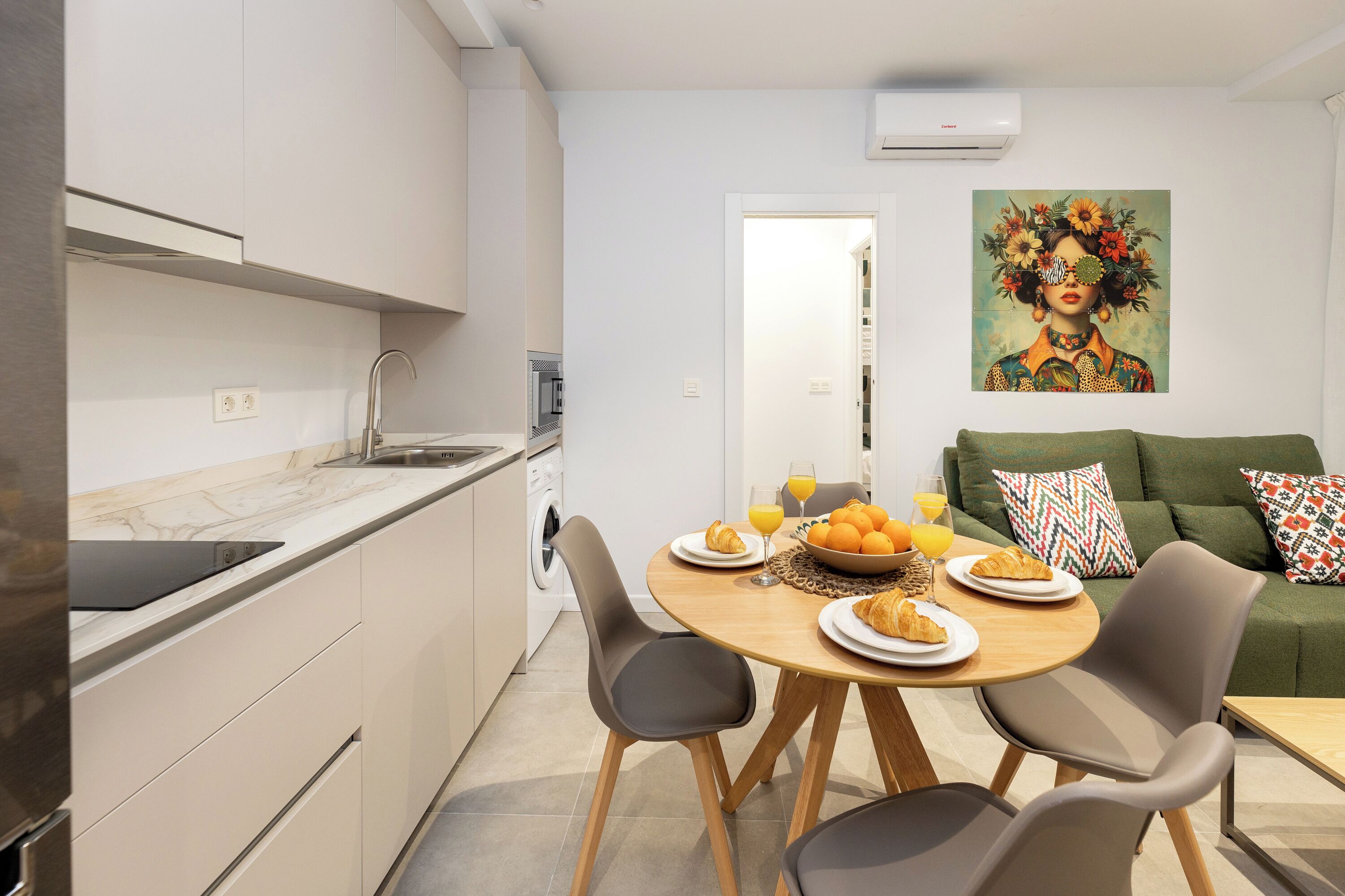 A modern kitchen with a dining area, a green sofa, and a painting on the wall.