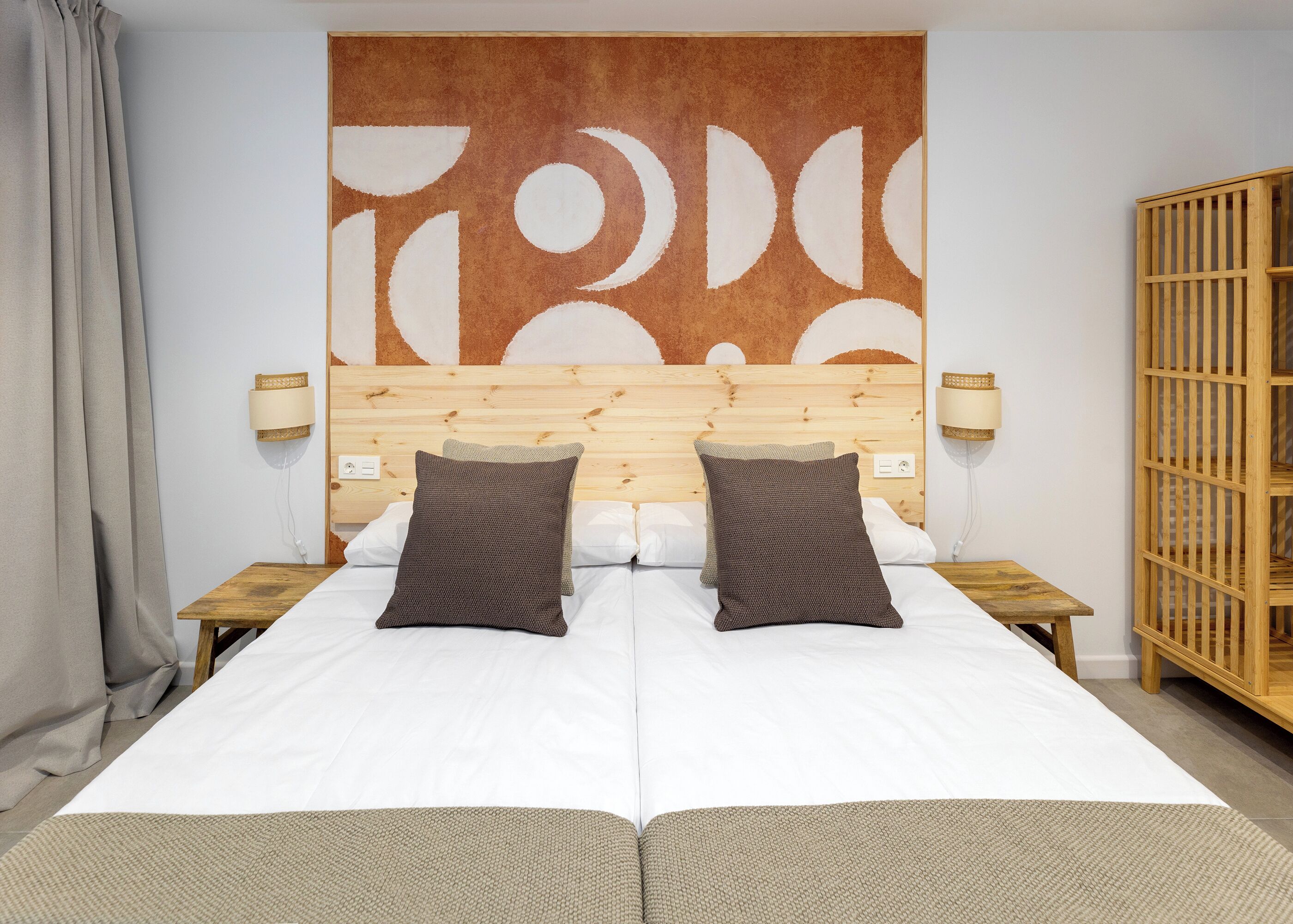 Un lit double avec deux oreillers, une tête de lit en bois, des lampes de chevet et une grande œuvre d’art abstraite accrochée au mur.
