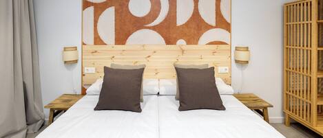 Un lit double avec deux oreillers, une tête de lit en bois, des lampes de chevet et une grande œuvre d’art abstraite accrochée au mur.