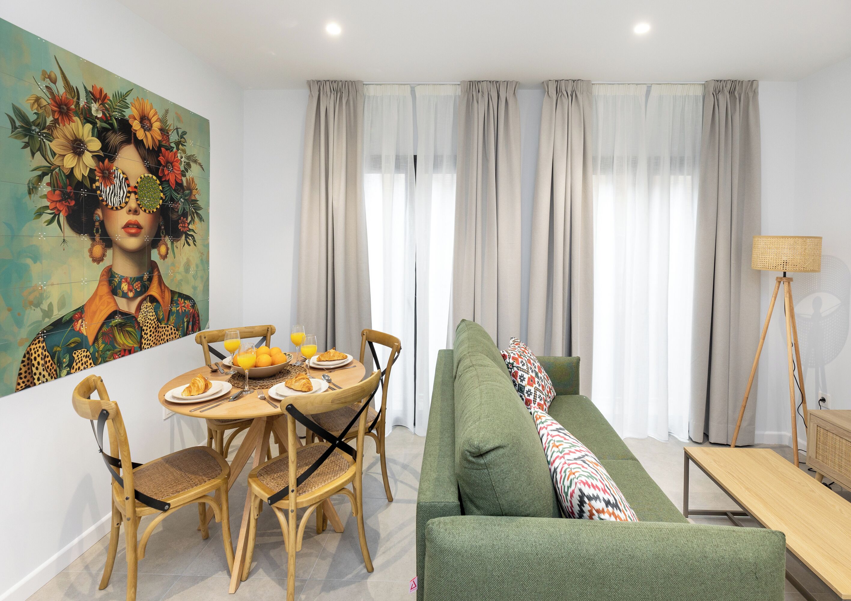 Un salon moderne avec un coin repas, comprenant un canapé vert, des chaises en bois, une table à manger avec des aliments pour le petit-déjeuner et un grand tableau accroché au mur.