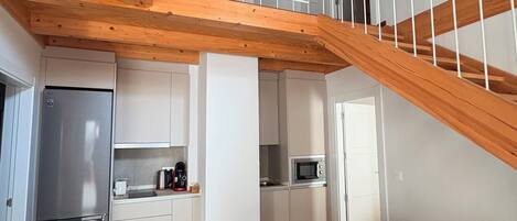 A modern kitchen with a central island, a dining area with a round table, and a wooden staircase.