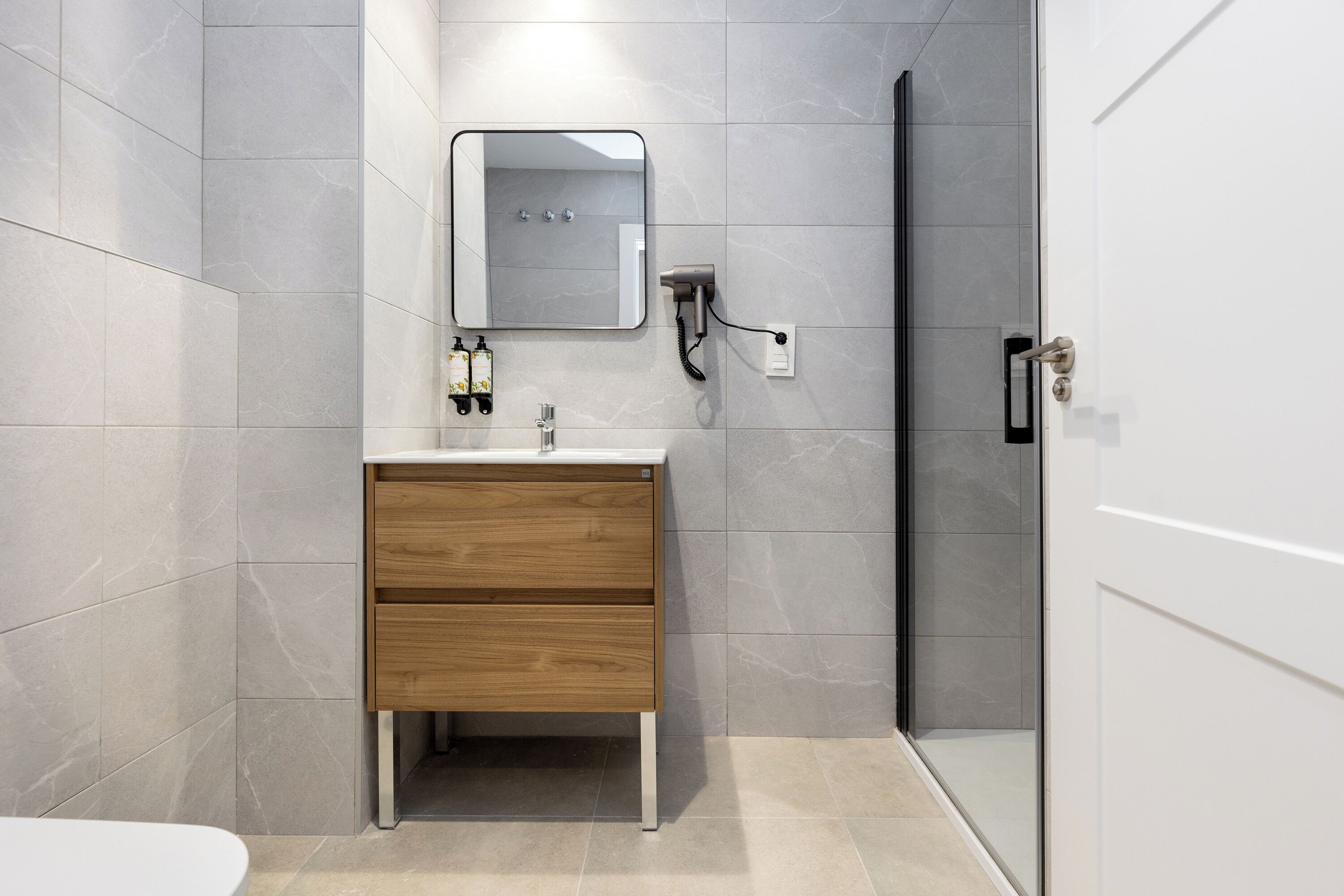 A modern bathroom with a wooden vanity, a mirror, a towel rack, and a shower area.