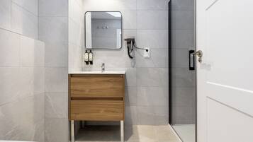 A modern bathroom with a wooden vanity, a mirror, a towel rack, and a shower area.