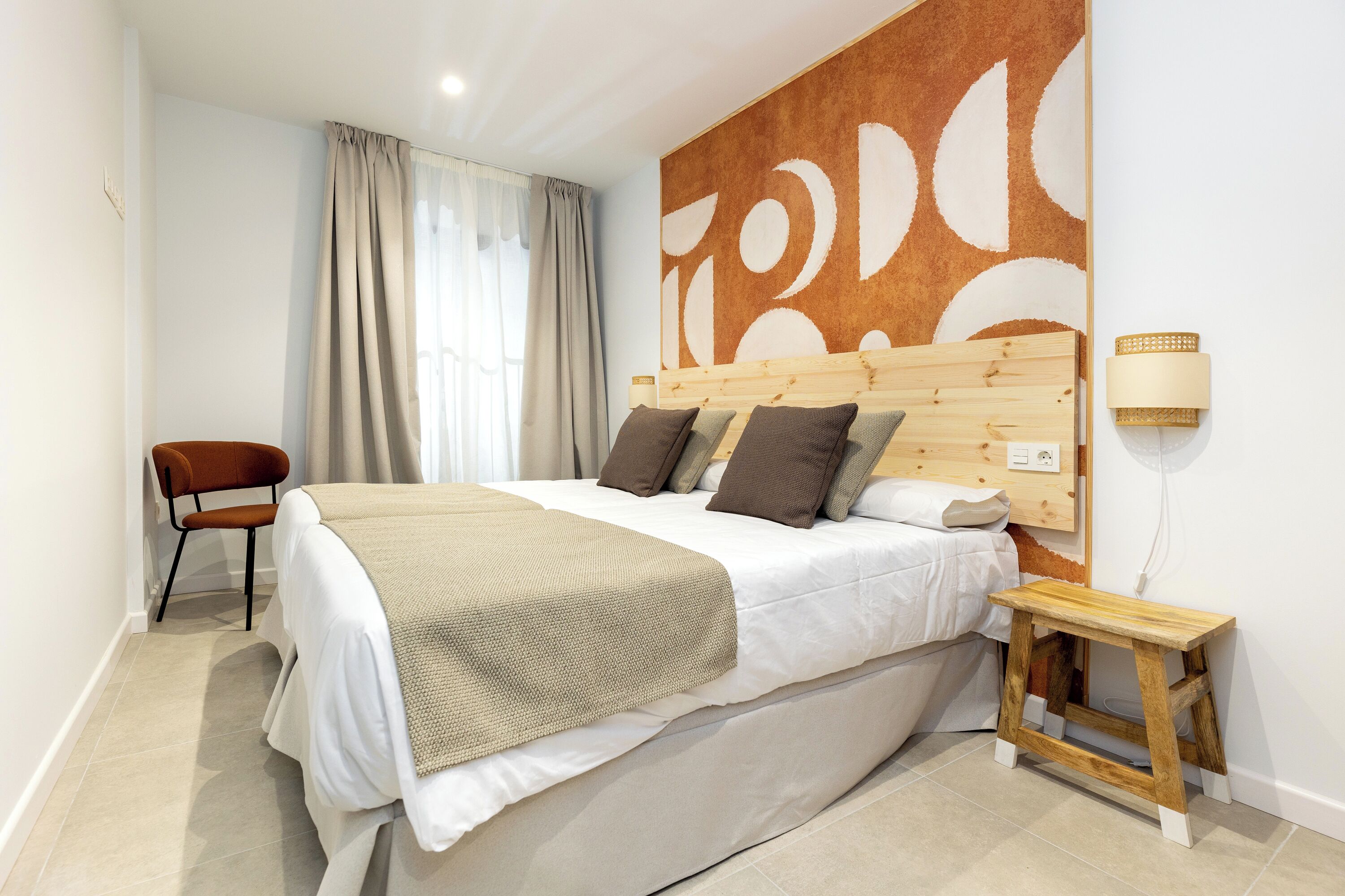 Un dormitorio con cama, una silla, una mesita de noche y una pared decorada con arte abstracto.