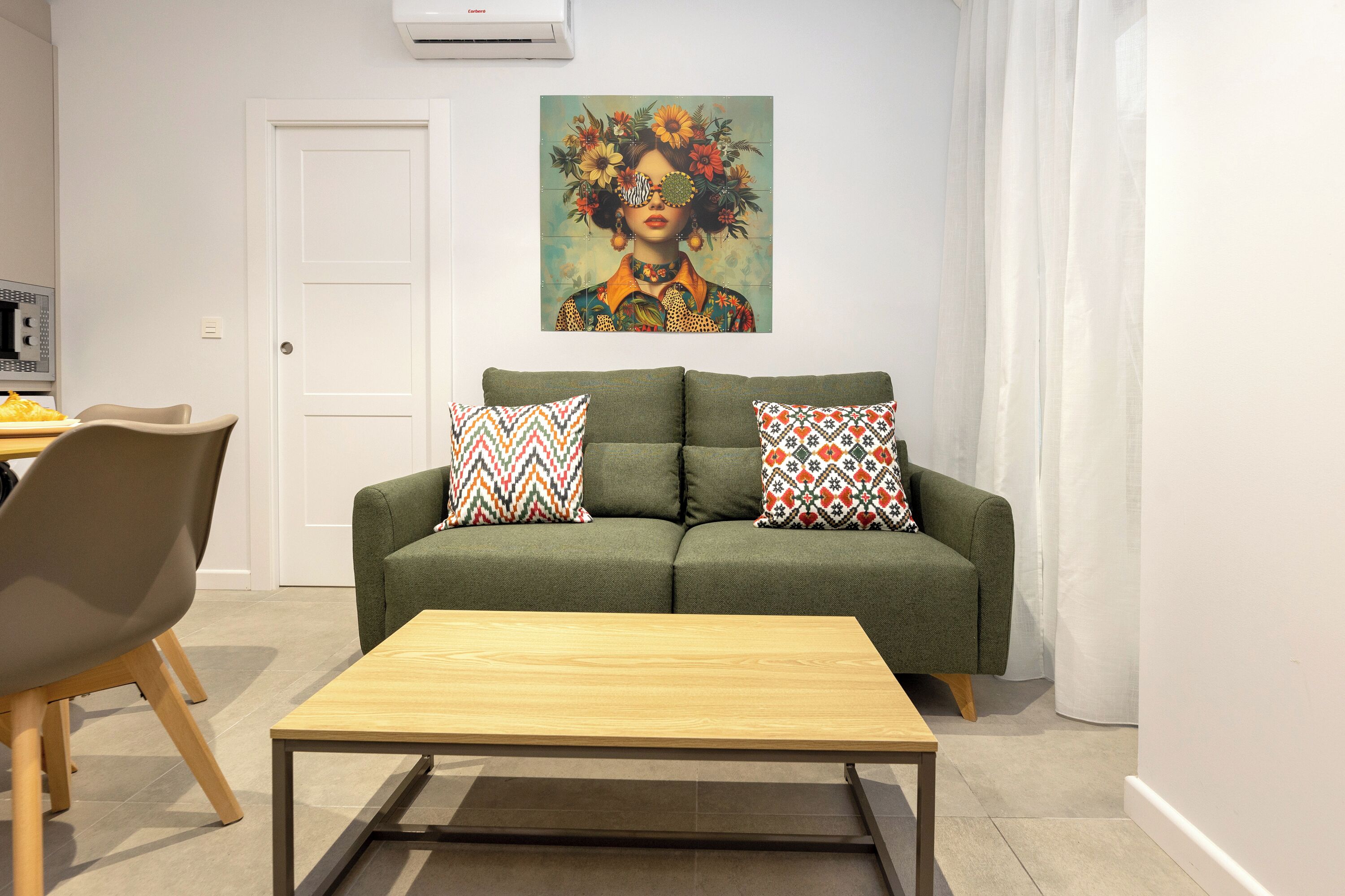 Un salon avec un canapé vert, deux coussins à motifs, une table basse en bois et un tableau accroché au-dessus du canapé.