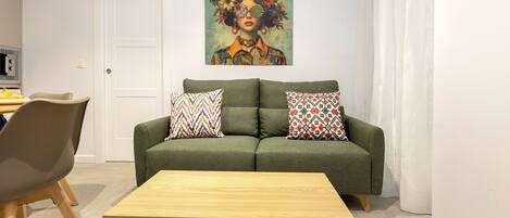 Una sala de estar con un sofá verde, dos almohadones estampados, una mesa de centro de madera y un cuadro sobre el sofá.