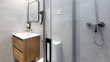 A modern bathroom with a wooden vanity, a white sink, a mirror, and a shower with a handheld showerhead.