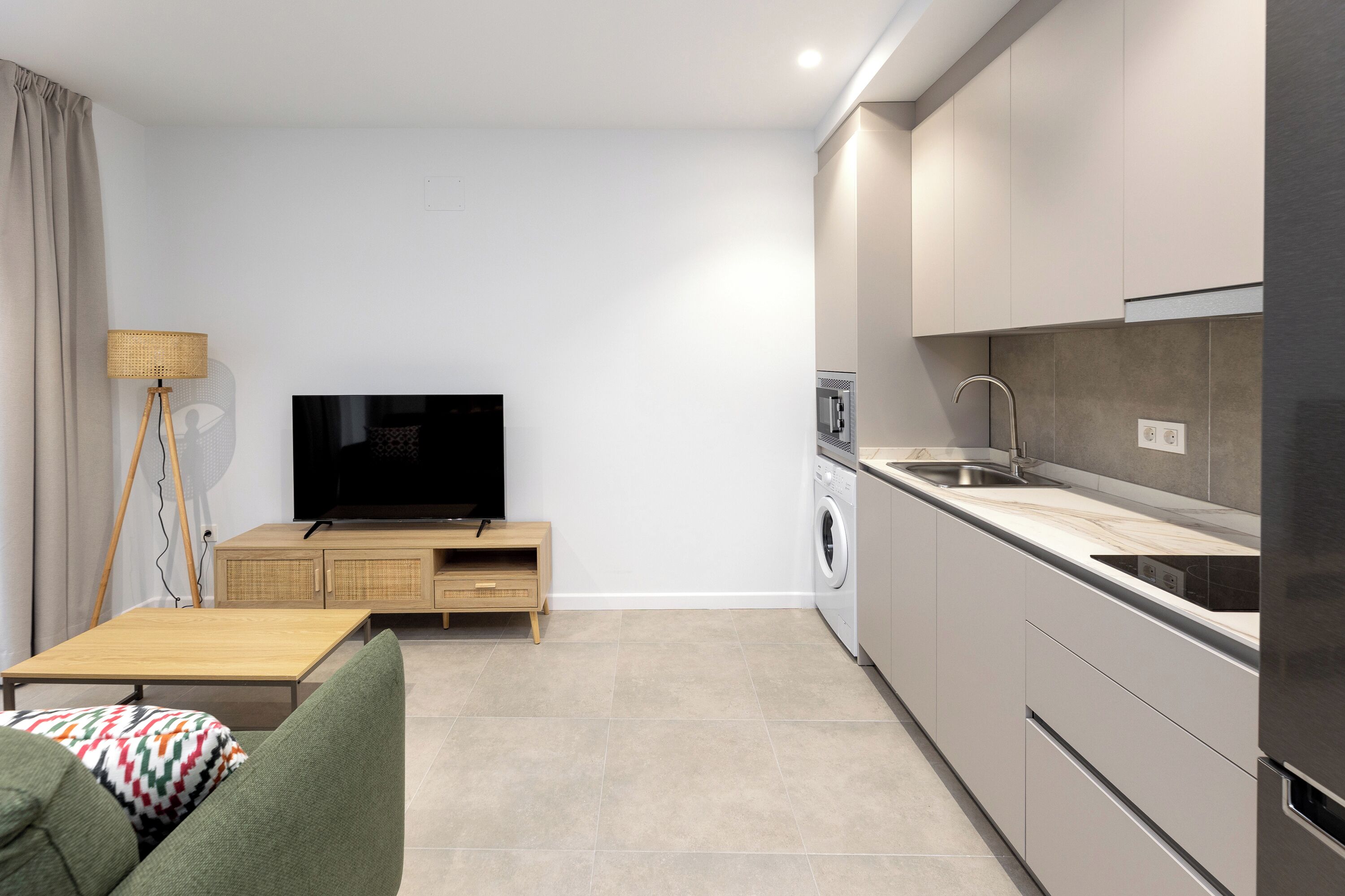 A modern kitchen with a flat-screen TV, wooden cabinet, and a washing machine.