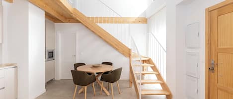 A modern kitchen with a dining area, wooden staircase, and white cabinetry.