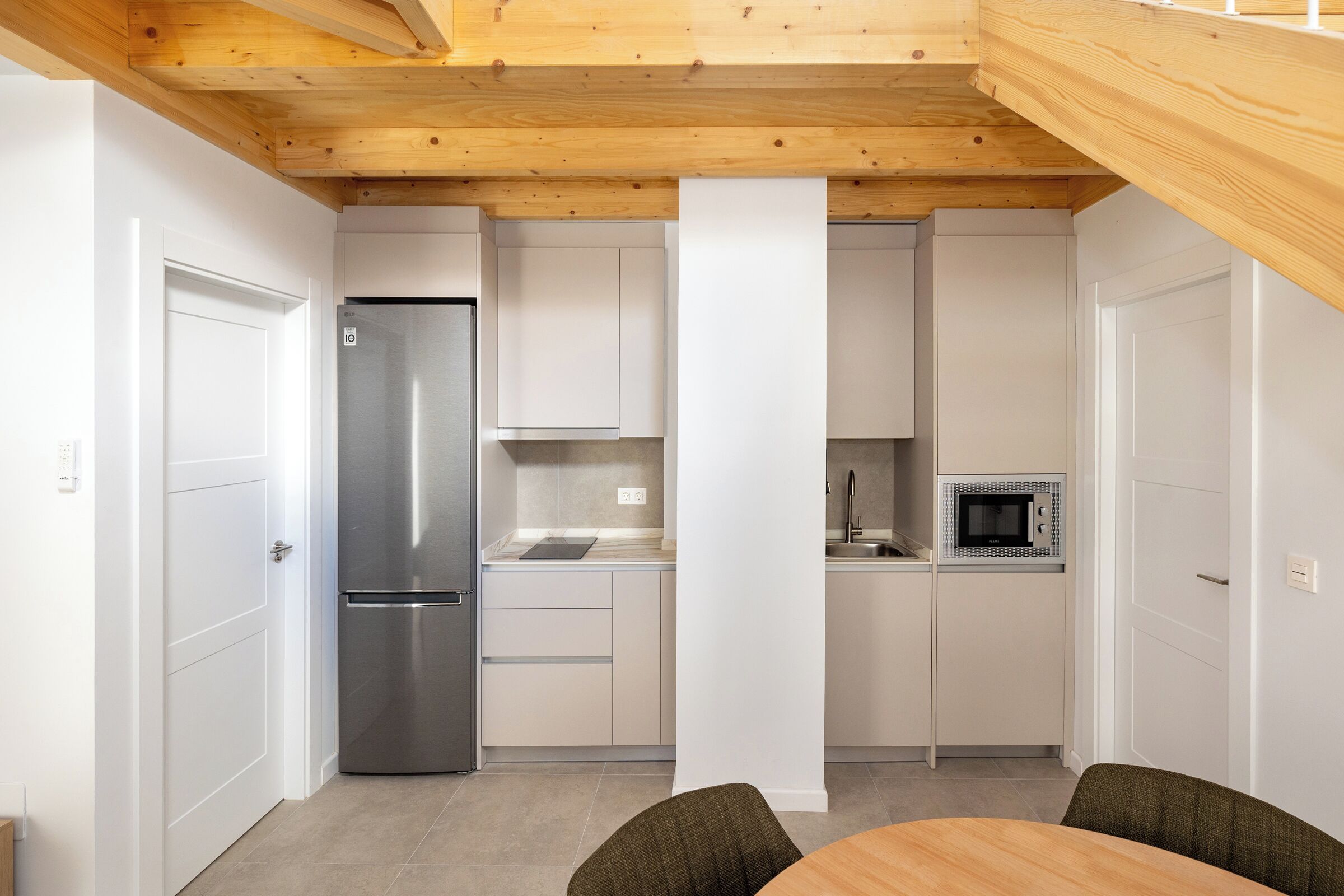 A compact kitchen with white cabinets, a stainless steel refrigerator, and a microwave.