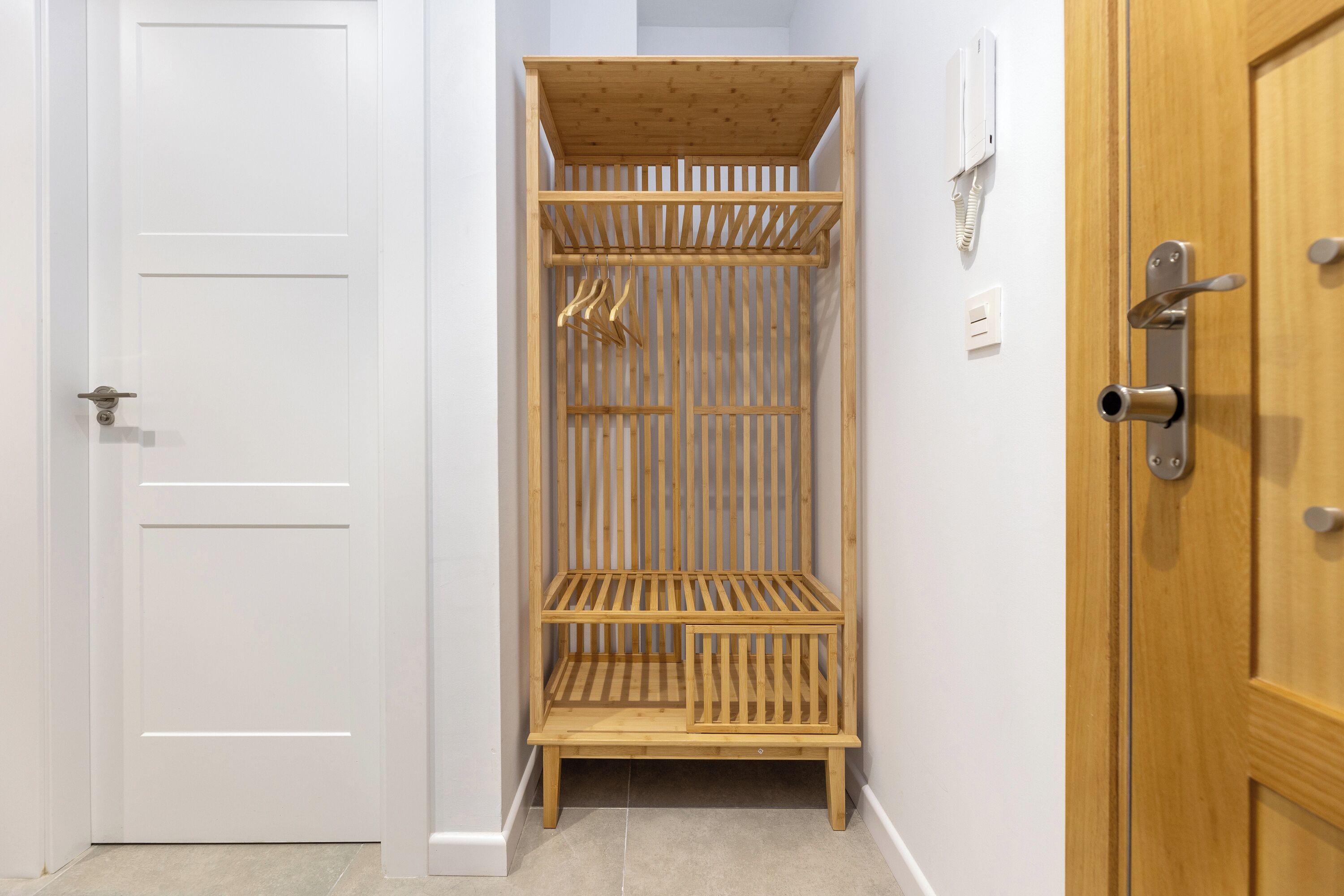 Una esquina de una habitación con una puerta blanca, un estante de madera y otra puerta de madera.