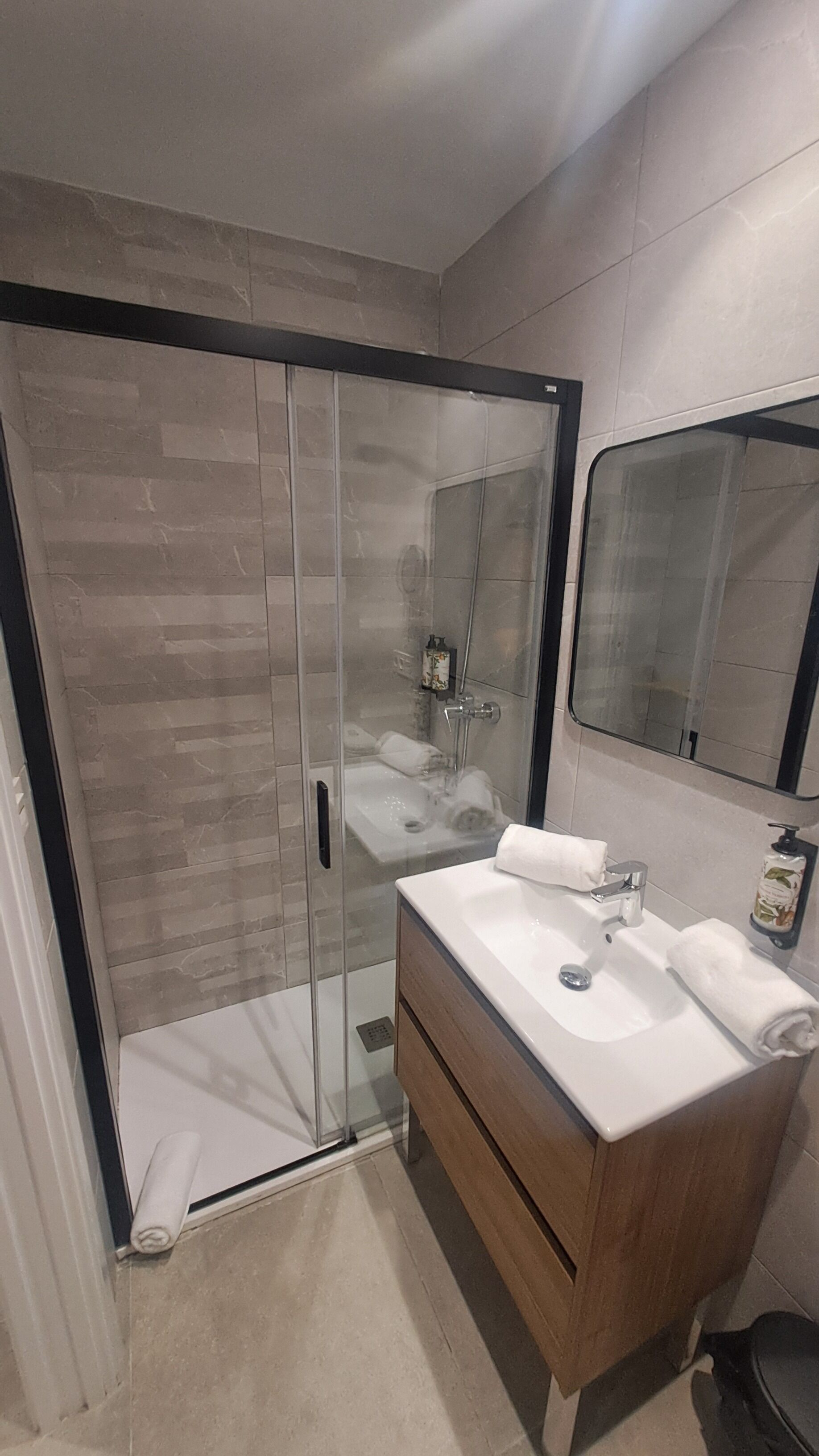 A modern bathroom with a glass-enclosed shower, a wooden vanity, and a large mirror.