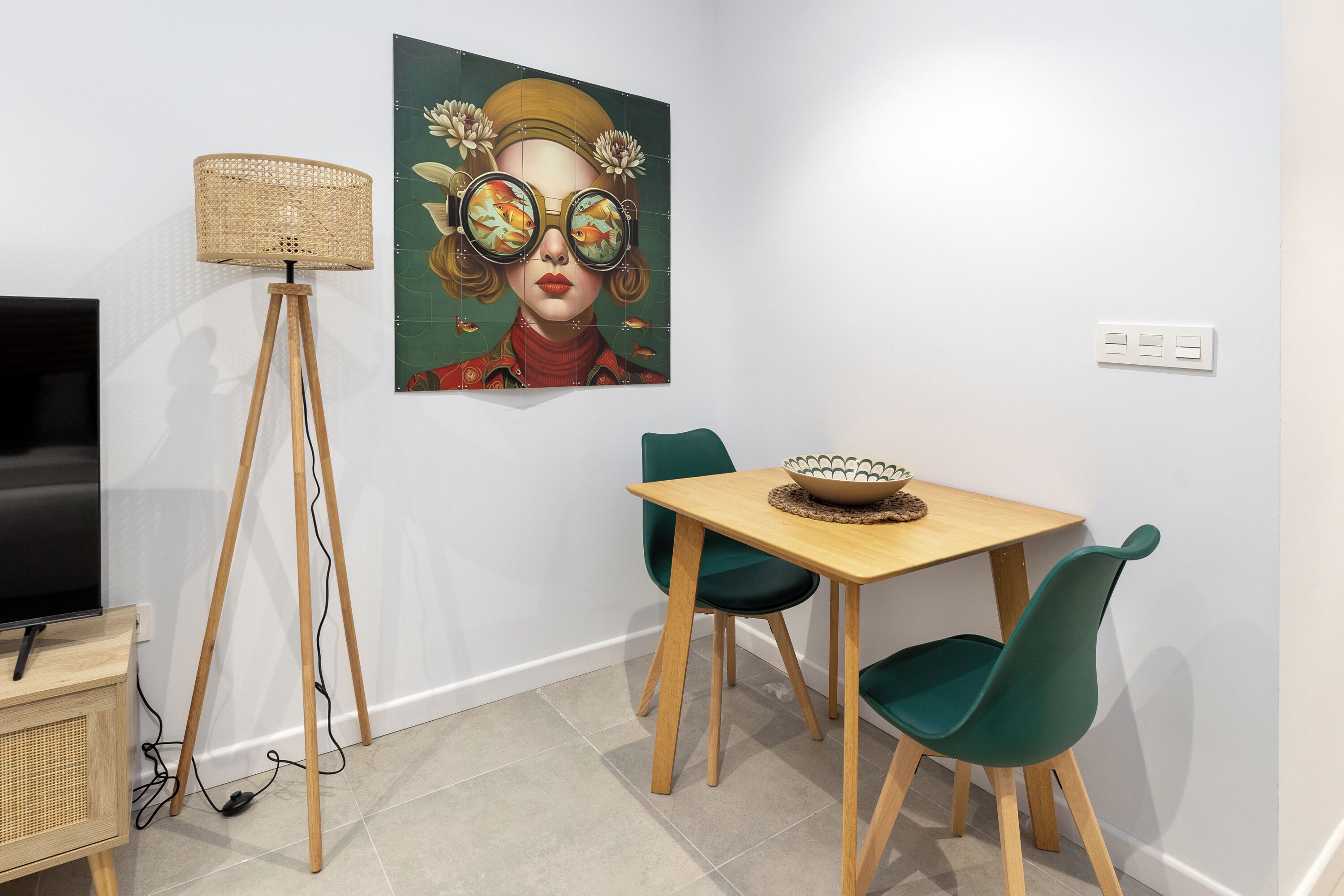 A dining area with a table, chairs, a lamp, and a painting on the wall.