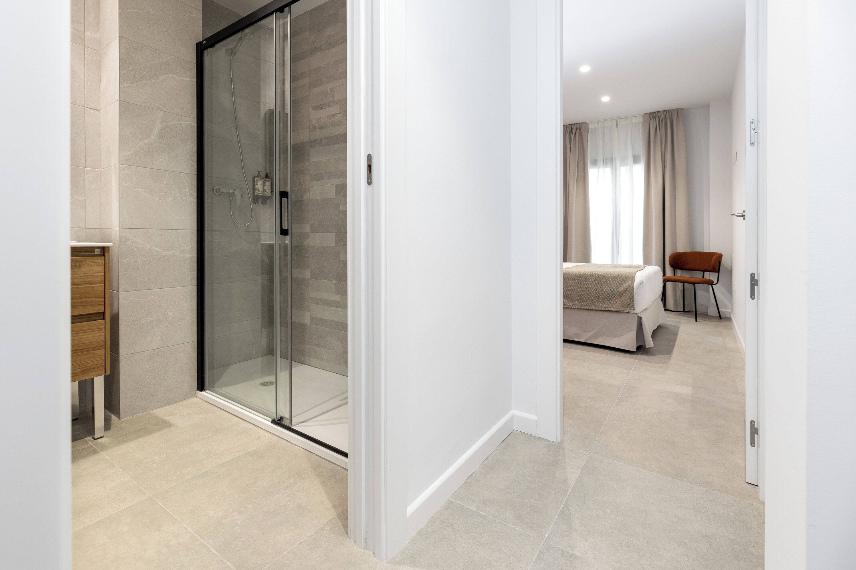 Una habitación de hotel moderna con cabina de ducha de vidrio, un mueble de madera y una cama con cubrecama blanco.