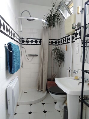 Compact bathroom with a shower, handheld showerhead, and separate toilet, featuring a black and white tile floor and diamond border.
