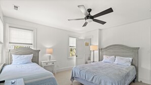 Un dormitorio con dos camas, ventilador de techo, lámparas de noche y una ventana con persianas.