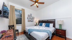 A hotel room with a bed, a TV, a ceiling fan, a window with curtains, a bedside table with a lamp, and a small table with a remote control. - Modern King bed Haven/Free parking, Pool, Balcony (Santa Rosa Beach)