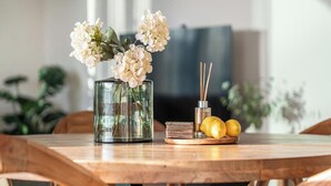 A dining table with a glass vase of flowers, a plate with lemons, and a set of candles.