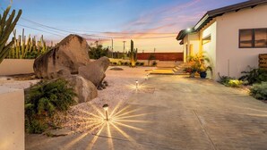 A modern house with a paved driveway, large rocks, and cacti.