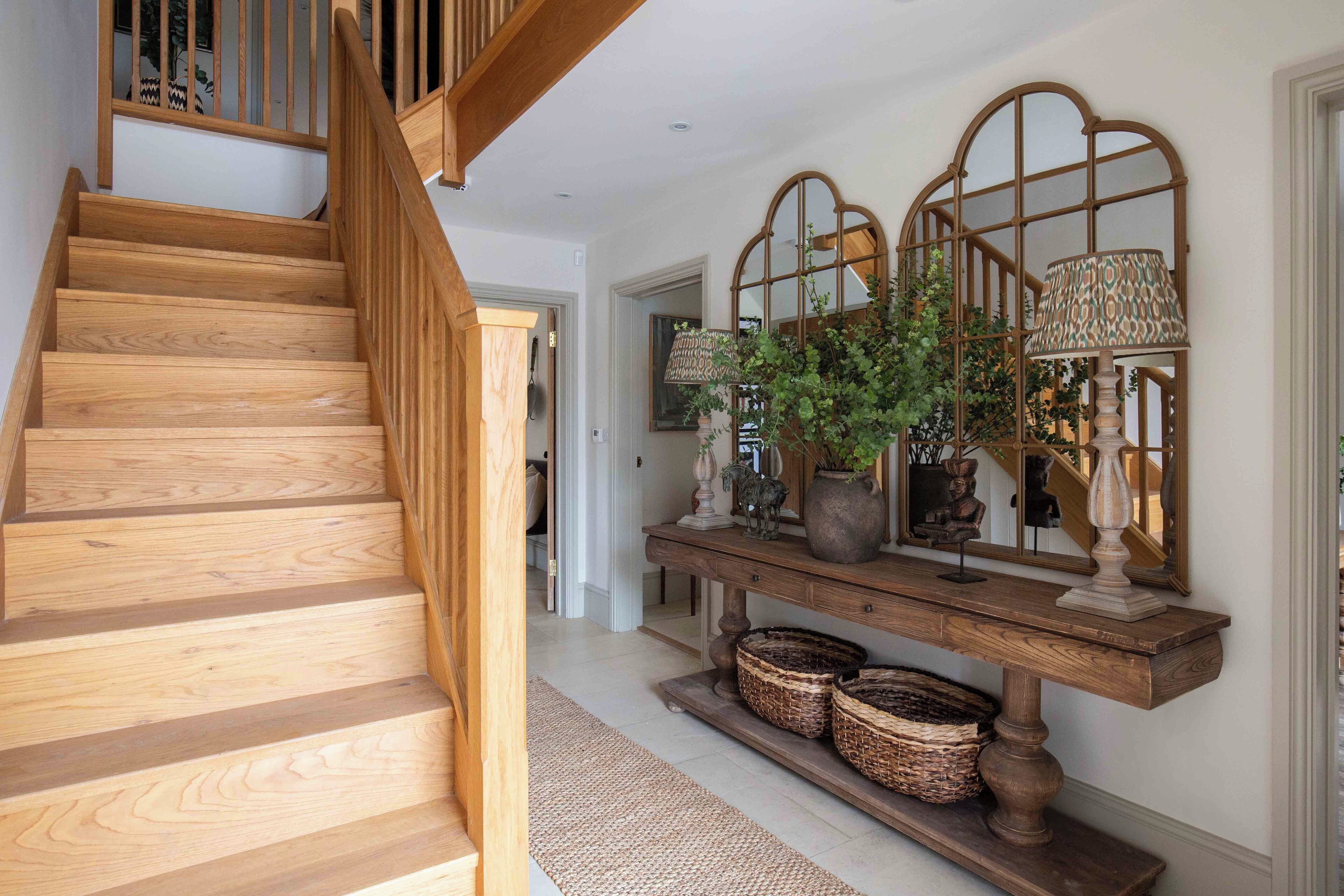 A wooden staircase leading to a landing with a console table, wicker baskets, and a mirror with a decorative frame.