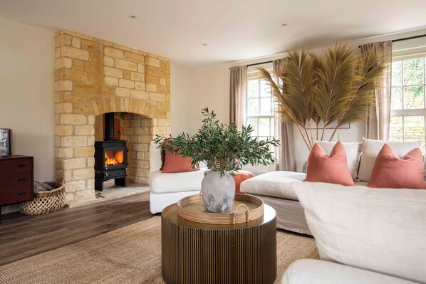 A living room with a stone fireplace, a sofa, a round wooden side table, and a potted plant.