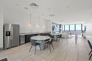 A modern kitchen with a stainless steel refrigerator, a marble island, and pendant lighting.