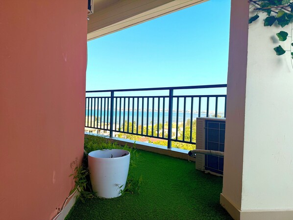 A balcony with a view of the sea, a white planter, and an air conditioning unit. - Posh Palm Village 3Bedroom Apartment (Dar es Salaam)