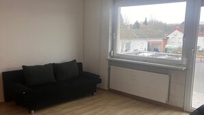 A room with a black sofa, a radiator, and a window with a view of buildings and trees. - NR 3 Apartment on the upper floor 3 ZKB for companies/families (Vellmar)