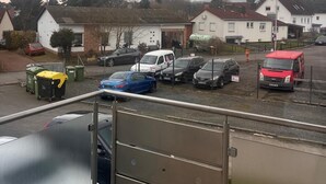 A view from a balcony overlooking a parking area with several cars, a red van, and residential buildings in the background. - NR 3 Apartment on the upper floor 3 ZKB for companies/families (Vellmar)