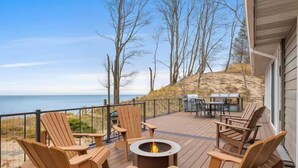 Eine Terrasse mit Holzstühlen und einem Feuerkorb, mit Blick auf einen Strand und den Ozean.