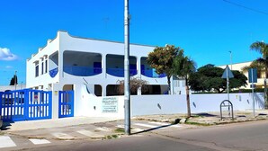 A white building with blue accents, a gated entrance, and palm trees in the background. - Villa Lea - Apartments Torre dell'Orso (Torre dell'Orso)