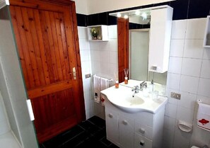 Un baño con puerta de madera, lavamanos blanco, espejo y paredes con azulejos.